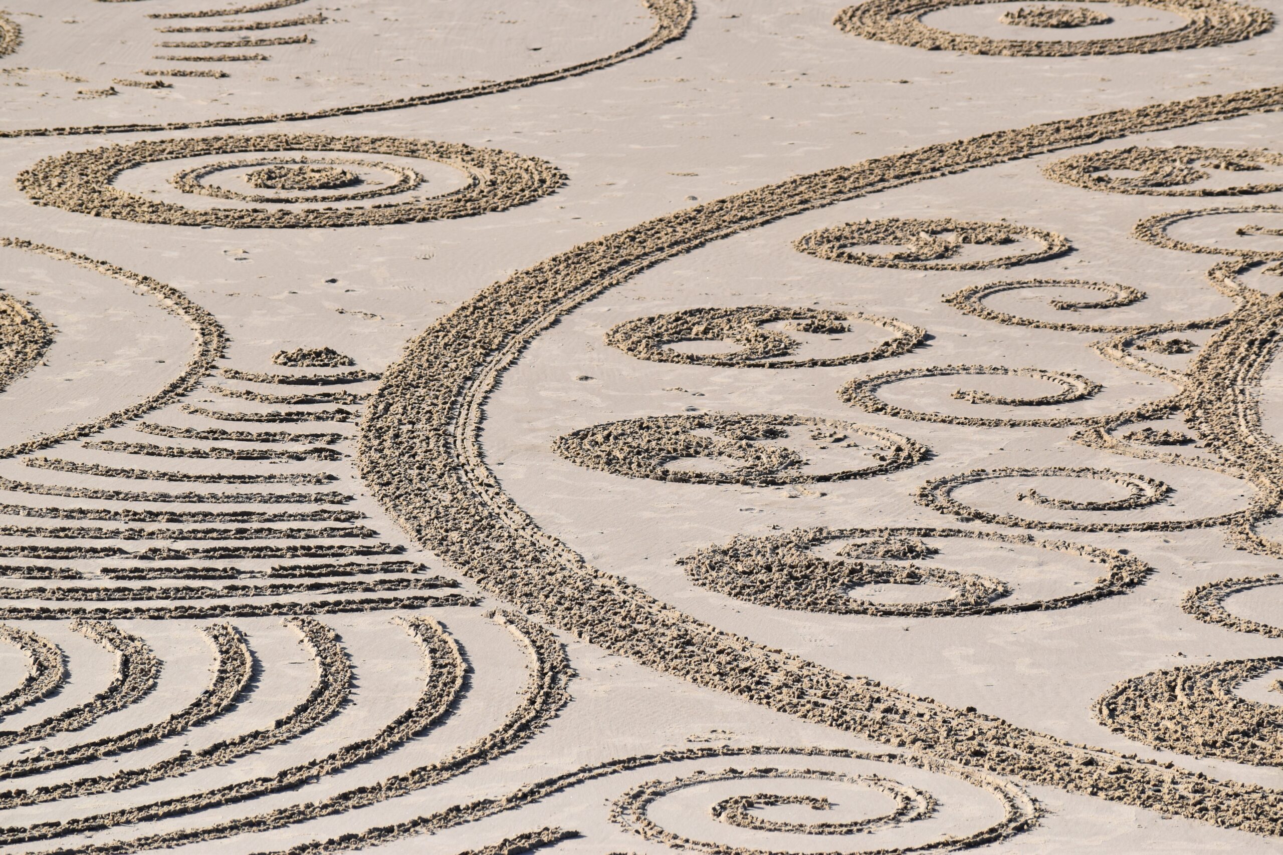 Photo by Jase Ess on Unsplash. Patterns drawn in the sand on a beach.